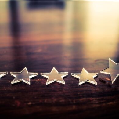 The best rating. Businessman arranging five transparent stars in row on a wooden desk. The office window is reflected on the desk